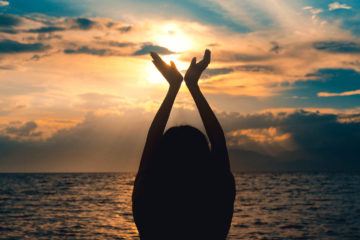 Femme mains levées devant coucher de soleil maritime